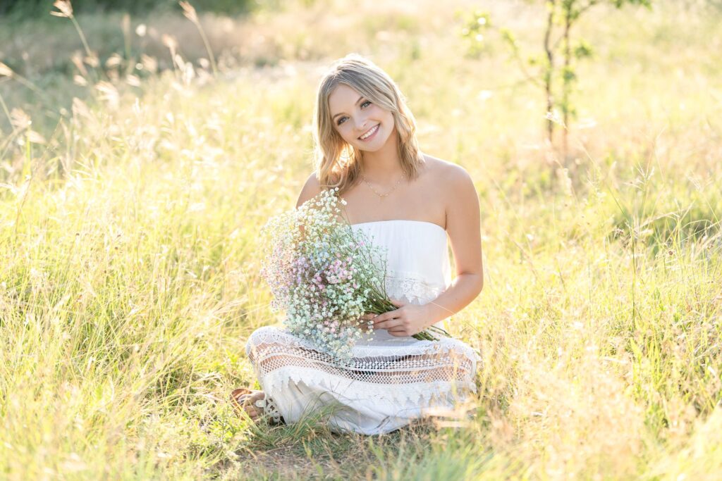 senior photo in a field with white dress and flowers
