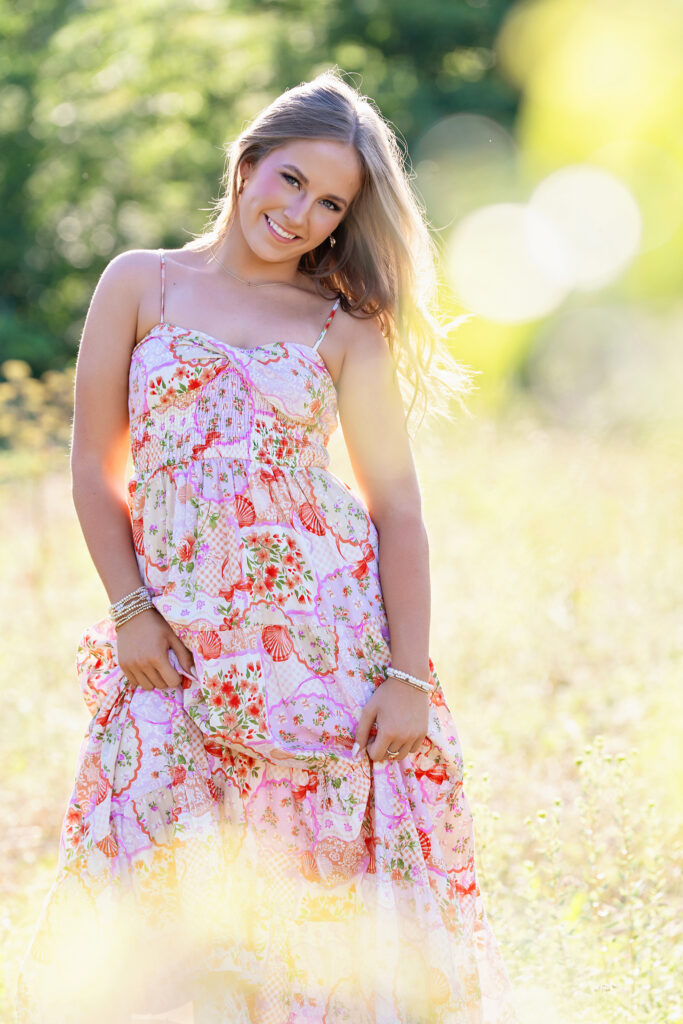 Spring senior photos in Fort Worth: senior girl in a pastel floral dress standing in a backlit wildflower field