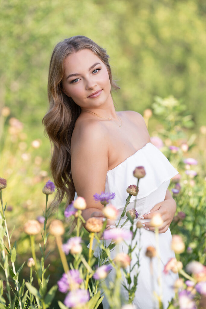 Senior girl in a white strapless dress standing among pink and purple wildflowers for spring senior pictures in Dallas-Fort Worth